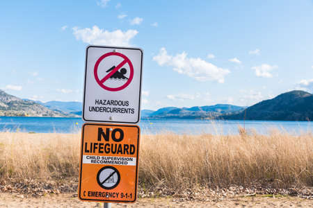 Water safety sign warning of hazardous undercurrents and no lifeguard with view of beach and lake