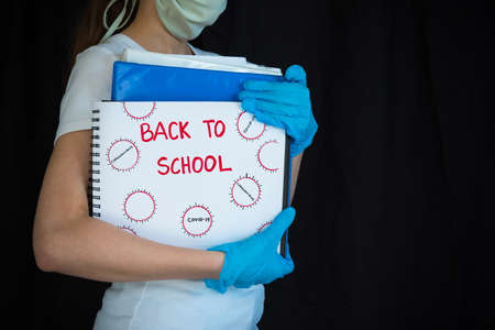 Student wearing face mask and surgical gloves and holding school books with Back To School written on notepadの写真素材