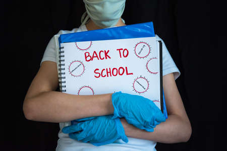Student wearing face mask and gloves, holding school books. Concept of reopening schools during COVID-19 pandemic.の写真素材