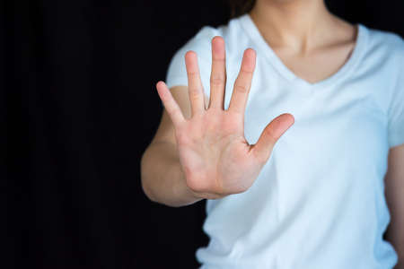 Woman holding out hand in stop gesture, with black background and copy spaceの写真素材