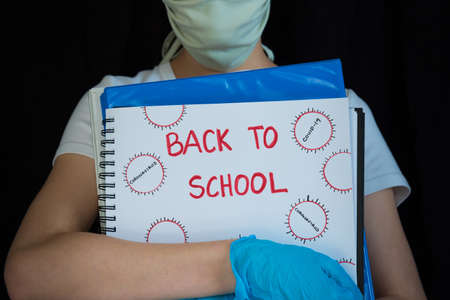 Close-up of student wearing face mask and surgical gloves, holding school books with Back to School written on coverの写真素材