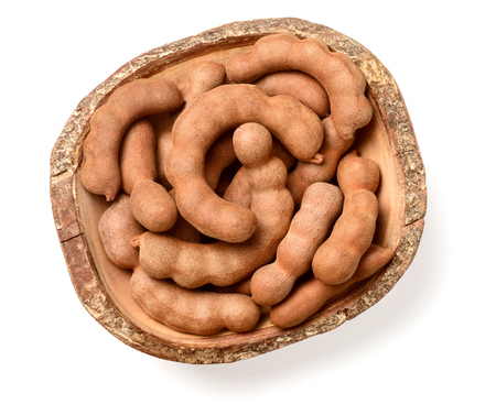 fresh tamarind fruits and leaves in the wooden bowl, isolated on the white background, top viewの写真素材
