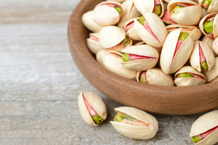pistachio nuts with shell in the wooden plate, on the wooden boardの写真素材