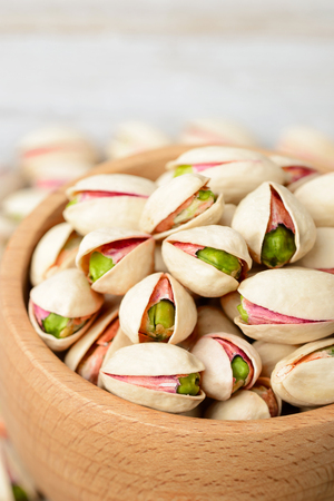 pistachio nuts with shell in the wooden bowl, on the wooden boardの写真素材