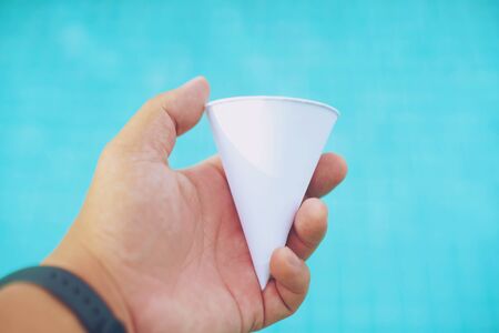 Mockup of male hand holding a filling a paper cup of waterの写真素材