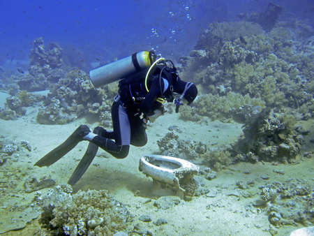 Unidentifiable diver bend over a scrap toilet underwater