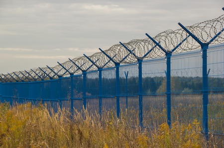 Blue fence with barbed wire in the field.の写真素材