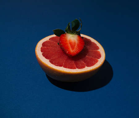 Fresh organic fruit citrus pink grapefruit slices with red strawberry on the royal blue background.の写真素材