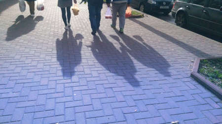 People with plastic bags and their shadows in the street.
