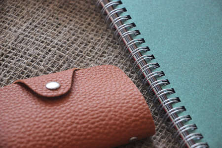Brown leather wallet and cdark green opybook on canvas top view.
