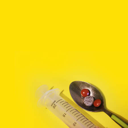 Pharmaceutical pills in spoon and syringe on a yellow background, square layoutの写真素材