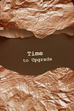 The words Time To Upgrate.appearing behind torn bronze foil. Business concept for updating somethingの写真素材