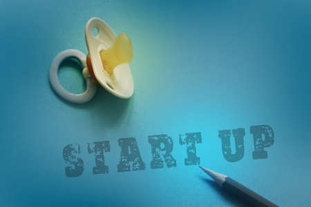 One blue plastic nipple pacifier soother on a blue background, wth words Start up, new business startup concept.の写真素材