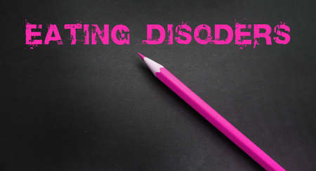 Eating disorder words written with pink pencil on dark background. Weightloss anorexia bulimia...