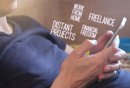 Work from home, freelance and Financial freedom words glowing from mobile smartphone screen in man's hand. Distant job online shop internet business concept.の写真素材