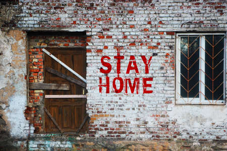Stay home inscription on old brick wall .sealed door and barred window. Self-isolation at home from a coronovirus concept.の写真素材