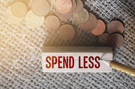 Spend less text on wooden block and coins on burlap. Saving money financial concept.の写真素材