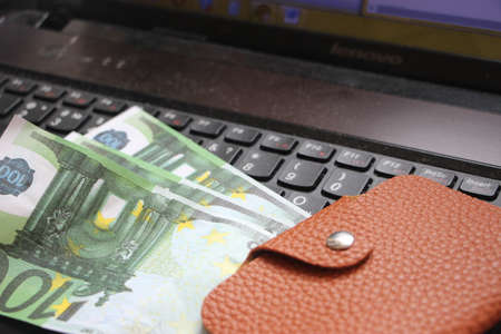 Brown leather wallet, some hundred euro banknotes on keyboard. Web shopping business concept with euro money.の写真素材