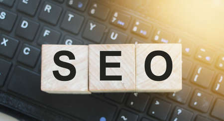 Wooden cubes with the acronym SEO for search engine optimization put on computer keyboard. Online...