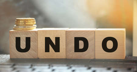 Undo word on wooden cubes with letters, and stack of coins. Technical issue computer program...