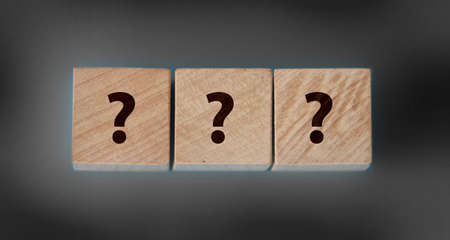 Wooden cube block shape with sign question mark symbol on black table.