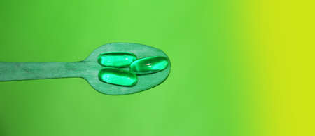 Green Neon Glow Gel Pills on wooden spoon. Addiction or healthcare concept.の写真素材