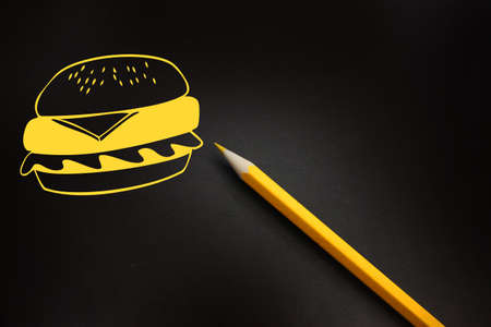 Hamburger icon-like drawing in yellow fast food on black board with yellow pencil besides. Fatfood...