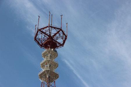 Top of high altitude Construction of TV tower painted into white and red under blue sky.