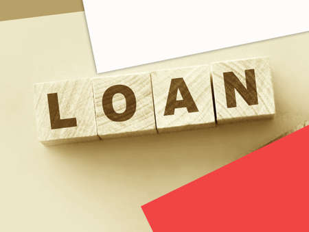 Wooden Blocks with the text: Loan with pink leather wallet besides on warm pink background. Finance...