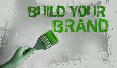 Build your brand words on gray wall with paintbrush in s hand. Motivational business marketing concept.の写真素材