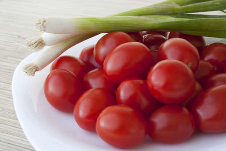 Small tomatoes with green onion on a plateの写真素材