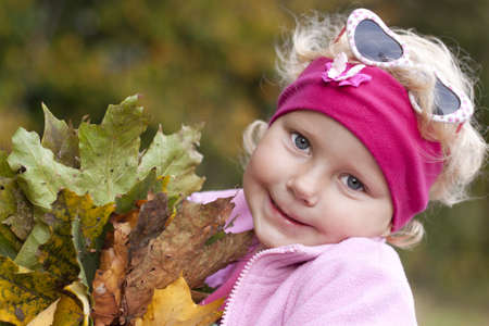 Little girl with a bouquet of autumn leaves in the parkの写真素材