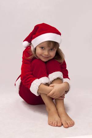 Pretty girl in a red dress Santa Claus sitting on the white backgroundの写真素材