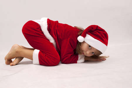 Girl in red Santa Claus costume curled up on the floorの写真素材