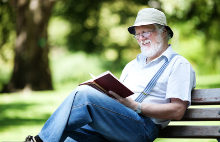 Senior male sitting in park enjoying a bookの写真素材
