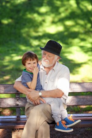 Grandson and grandfather relaxing on the park bench, shallow depth of fieldの写真素材