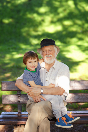 Grandson and grandfather relaxing on the park bench, shallow depth of fieldの写真素材
