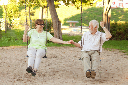 Senior couple having fun on park swingsの写真素材