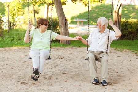 Senior couple having fun on park swingsの写真素材