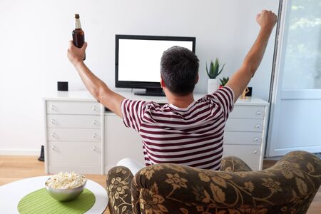 Image of a young man watching sports on TV, cheeringの写真素材