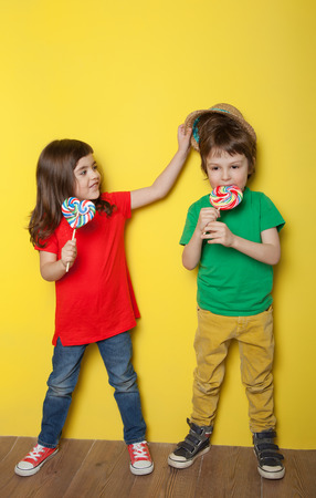 Adorable boy and girl having great time while licking lollipops, on red and yellow backgroundの写真素材