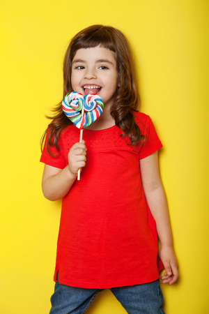 Adorable girl licking lollipop, on yellow backgroundの写真素材