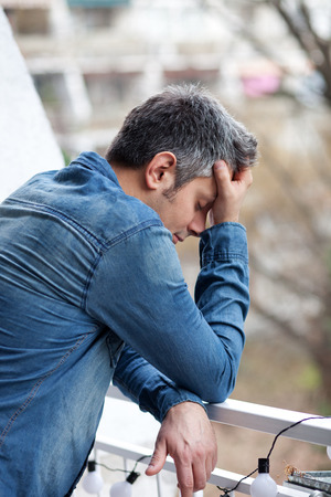 Portrait of depressed young man standing on balconyの写真素材
