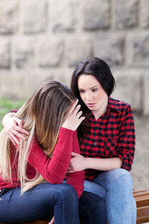 Young girl consoling her sad friend outdoors