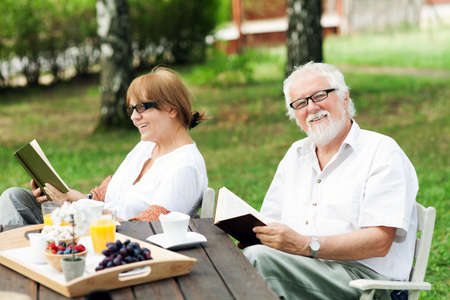 Senior couple reading books in the garden, shallow depth of fieldの写真素材