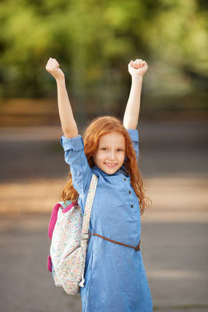 Adorable little red-haired girl posing with books and backpackの写真素材