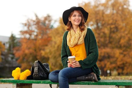 Portrait of young woman holding a bunch of yellow flowers and cup of coffee, shallow depth of field