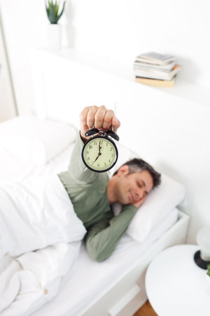 Man extremely annoyed by the alarm clock, shallow depth of field, focus on foreground