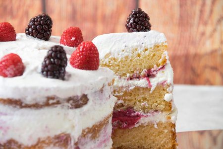 close up of a sliced sponge cake filled with whipped cream and berries sauce topped with blueberries...