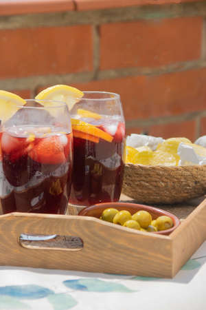 Two crystal glasses filled with red wine and soda with ice cubes and slices of lemon typical spanish on a wooden tray with a plate of olives and a bowl of potato chips on a brick wall background. Sangria concept.の写真素材